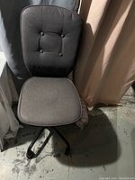 Photo of a black fabric computer chair showing cushioned seat and backrest with button detail, and height adjustable base.