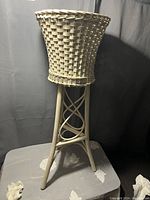 Floor model wicker planter on stand with woven basket design and curved top edge.