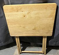 Front view of a folding wooden TV tray against a dark background showing the natural wood surface and folding legs.