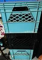 Photo of two stacked plastic milk crates, one turquoise and one black, showing lattice design sides and solid panels