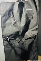Front view of a black fabric suit bag with Moores logo and clear ID pocket, showing handle and zipper closure.