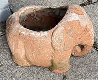 Ceramic planter in the shape of an elephant with an open cavity for planting. Shows some weathering and discoloration.