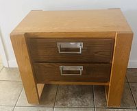 Wooden retro side table with two drawers and metal handles, light-colored legs and darker front drawer panels.