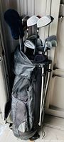 Full view of the black and gray golf carrying bag with multiple golf clubs inside, including irons, woods, and putter visible, some clubs with headcovers (blue fuzzy and black fabric covers).