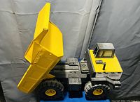 Side view of the metal Tonka dump truck showing yellow raised bed lifted, black chassis with large black wheels, and yellow cab with black and gray details.