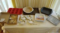 Wide view of all bakeware laid out on table in natural light, includes various pans, cookie cutters, grater, measuring spoon