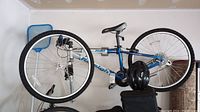 Blue Raleigh M40 bike hanging on rack, shows full side profile including tires, frame, seat, and handlebars with black helmet attached to frame.