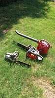 Overview of two chainsaws and one leaf blower placed on grass outside. One chainsaw is Craftsman brand with red and black colors; the other chainsaw is rusted and older model. The leaf blower is red and labeled Homelite.
