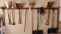 Photo of garden tools hanging on wall, including shovels, rake, and electric hedge trimmer