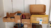 Several cardboard boxes on shelf containing various hand tools and miscellaneous items