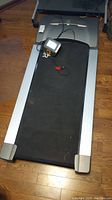 Full view of black iMovR treadmill with silver frame edges and controller on hardwood floor.