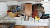 Shelf view showing various tools, grinding disc, gloves, brushes, cardboard box and plastic tray with hardware and tools.