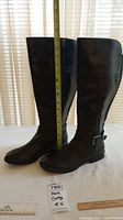 Pair of two black Marc Fisher women's boots placed side by side with a measuring tape showing their height approximately 17 inches.