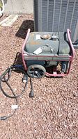 Front view of portable generator on gravel surface, showing fuel tank, frame, and wheels.