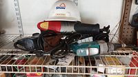 Photo showing red and black Skil Sawzall, teal and black power tool, and white Shaw hardhat on metal shelf