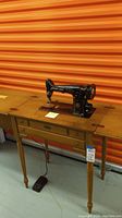 Full view of vintage Singer sewing machine mounted on wooden cabinet with turned legs.