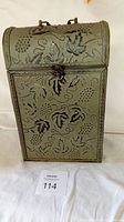Front view of stamped tin two-bottle box showing embossed grape motif, latch, and handle