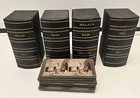 Photo showing four black storage boxes with gold lettering labeled England Vol. 1, France, Malaya Siam Ceylon, and China Vol. 1, along with a small stack of stereoview cards in front.