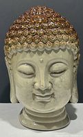 Front view of ceramic Buddha head with brown curled hair, serene facial expression, closed eyes, and urna on forehead.