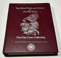 Closed view of maroon hardcover album titled 'The Official Birds and Flowers of Our Fifty States First Day Cover Collection' with silver embossed illustration of bird and flower.