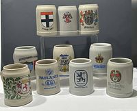 Front view of all 10 ceramic beer steins with various city and brewery crests and logos in multiple colors.