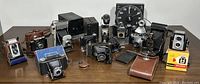 Full view of the collection of vintage cameras including folding, box, and other styles on a wooden surface