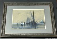 Framed watercolour painting showing a harbour scene with boats moored and people near the water reflecting on the surface, displayed in a decorative dark frame with a grey mat.