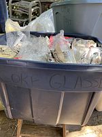 Grey bin labeled 'Coke Glasses' filled with bubble wrapped Coca-Cola glasses wrapped in newspaper.