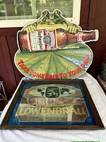 Budweiser frog sign featuring a frog holding a beer bottle over a leaf with red text displayed on a table.