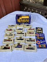 Lot of collectible die-cast cars and buses, most in original boxes or packaging, laid out on a white cloth surface.
