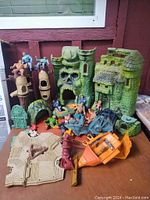 Image showing the large Castle Grayskull playset with several Masters of the Universe figures positioned around it along with vehicles and accessories, providing an overview of the lot.