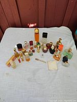 Overview of 25 vintage perfume bottles on white cloth in front of a red wooden wall. Shows variety of glass types, heights, and caps. Includes some vintage packaging and dropper applicator.