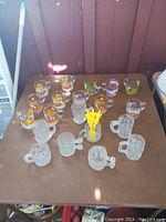 Overview of all mugs on table showing Garfield mugs, clear textured mugs, and plastic container with stirrers