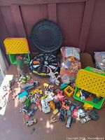 Image of multiple miniature Matchbox-like cars, dinosaur toys, plastic containers, and bags of toy parts spread on a flat surface.