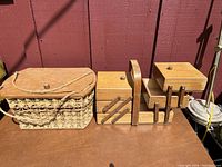 Two wooden items arranged side by side: a woven picnic basket with a wooden lid and rope handle on the left, and a multi-tiered wooden sewing box with compartments open on the right.