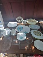 Wide view of all Pyrex and glass items on a brown table showing floral designs and clear glass pieces.