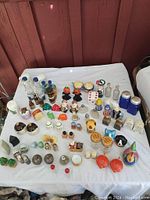Full view of the collection on a white cloth including many salt and pepper shakers in various styles and colors