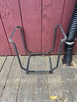 Angle view of metal firewood holder placed on wooden surface beside red painted wall and black corrugated pipe.