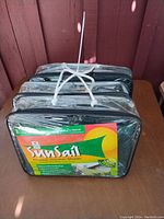 Shows three Sun Sail flexible garden shade panels, each in clear zippered packaging with green and yellow label.