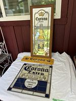 Photo showing framed mirror sign with Corona Extra bottle image, small yellow metal sign with Corona Extra text, and stained glass style sign beneath