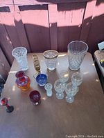 Photo showing all glassware pieces laid out on table under sunlight, including colorful vase, crystal vases, colored and clear glasses.