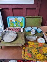 Wide shot showing all vintage trays and dishes from multiple angles. Includes metal trays, glass and ceramic dishes arranged on a table.