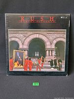 Front cover of Rush Moving Pictures vinyl LP showing figures with framed pictures in front of a stone archway building.