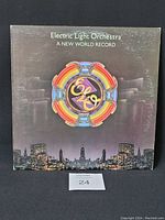 Front cover of Electric Light Orchestra's 'A New World Record' vinyl LP showing colorful logo and cityscape background.
