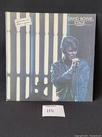 Front cover of the David Bowie 'Stage' double LP with a photo of Bowie singing, light bar pattern in background, sticker noting 2 record set with 20 songs.