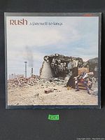 Front cover of Rush 'A Farewell to Kings' LP album showing artwork of ruined building and man in purple suit.