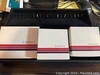 Three Eaton's branded boxes on black display case tray, unopened.