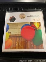 Front cover showing the 2012 Happy Birthday coin inserted in a slot above festive balloon imagery and text in English and French.