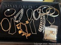 Top view of the black tray holding multiple bracelets and bangles with varying styles and materials including chain bracelets, plated silver, and mother of pearl inlay along with a rhinestone brooch.