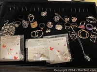 Full display of assorted jewelry laid out on black velvet including rings, bracelets, earrings, and two unopened Shiborui butterfly necklaces.